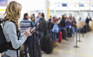 female traveller texting at airport check-in desk